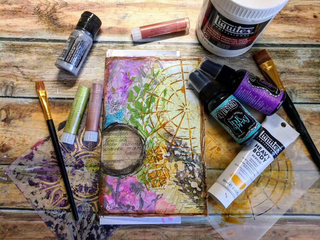 A painted art journal page with bottles of ink and paint scattered on the desk around it