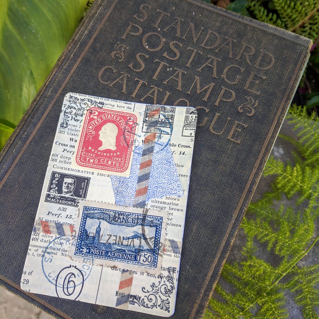 An old stamp catalog is in the background with an ATC lying on top of the cover