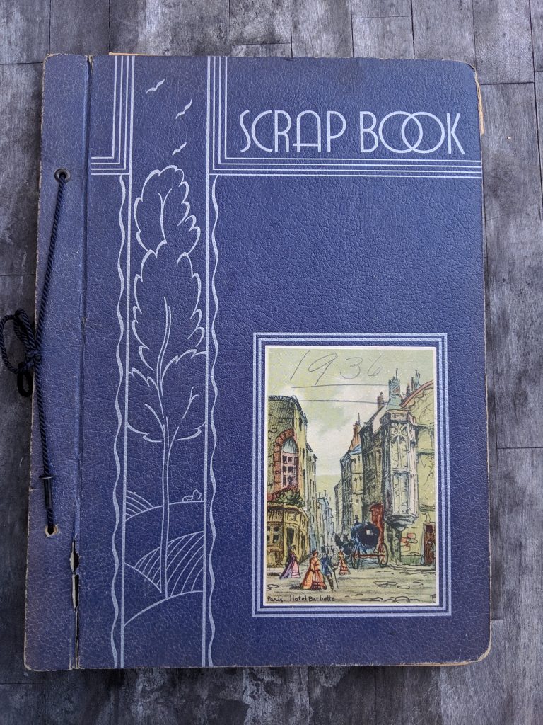 A blue cover with the word "Scrap book". An illustration decorating the bottom corner has the date 1936 written in pencil